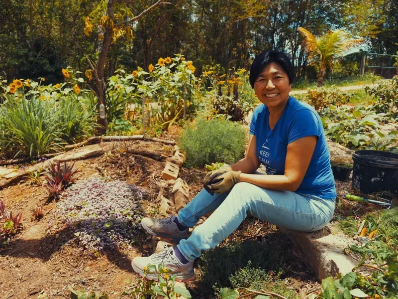 Member smiling beside a bed in the Monastery vegetable garden